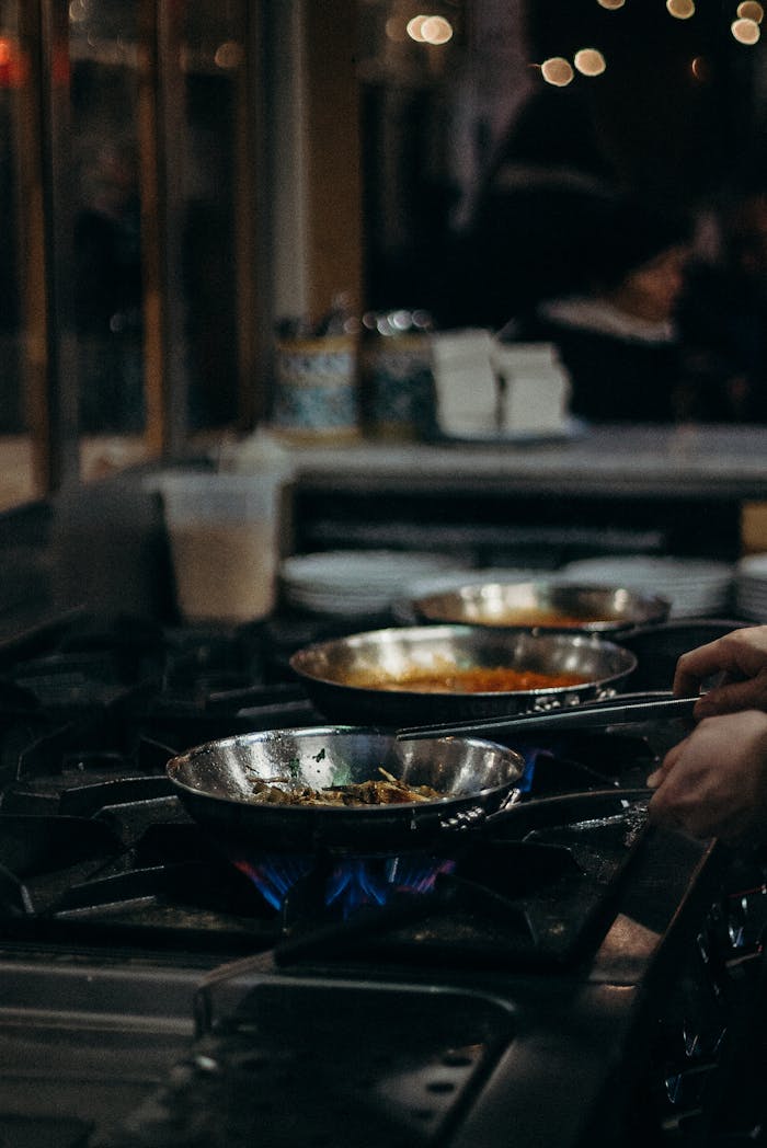Mastering the First Impression: Your intriguing post title goes here A chef expertly handles frying pans over open flames in a bustling kitchen setting.