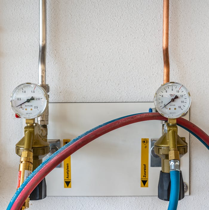 get-in-touch Close-up of industrial gas pressure gauges connected with hoses against a white wall.